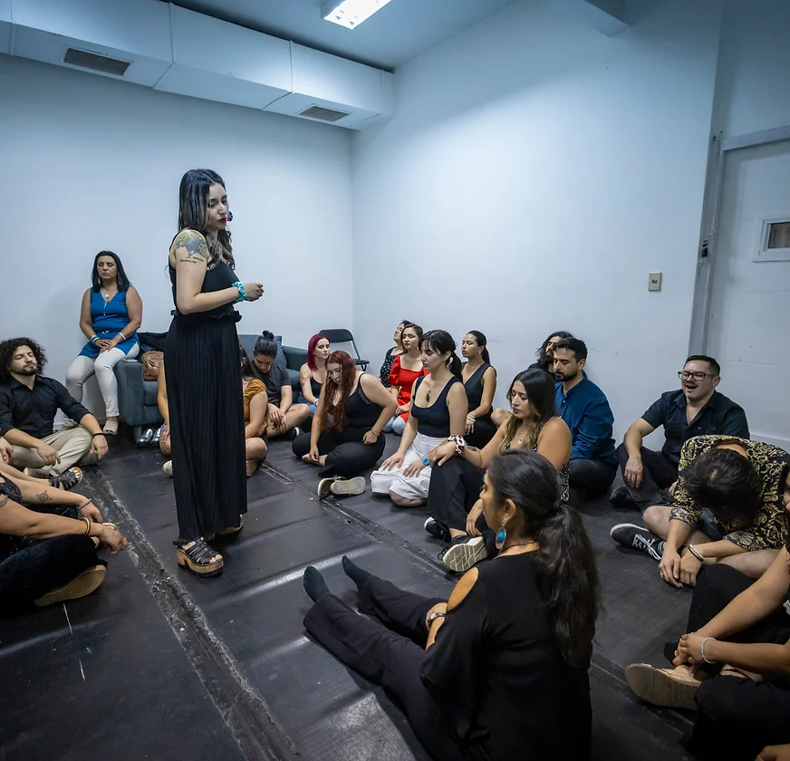 Mujer parada en el centro de una habitación, enseñandole a músicos técnicas para controlar la ansiedad escénica.